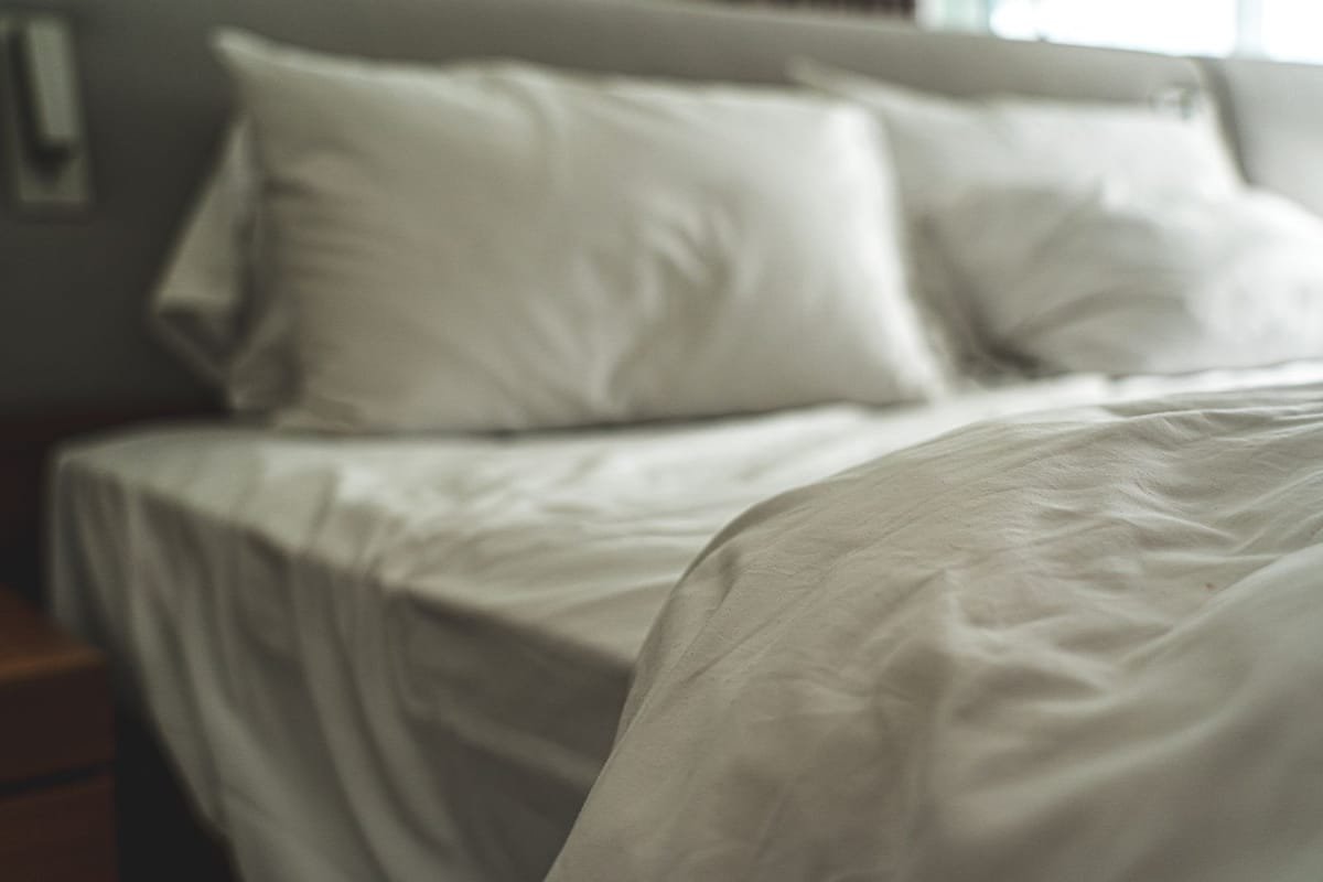 Cama de hotel arrumada com lençóis e travesseiros brancos