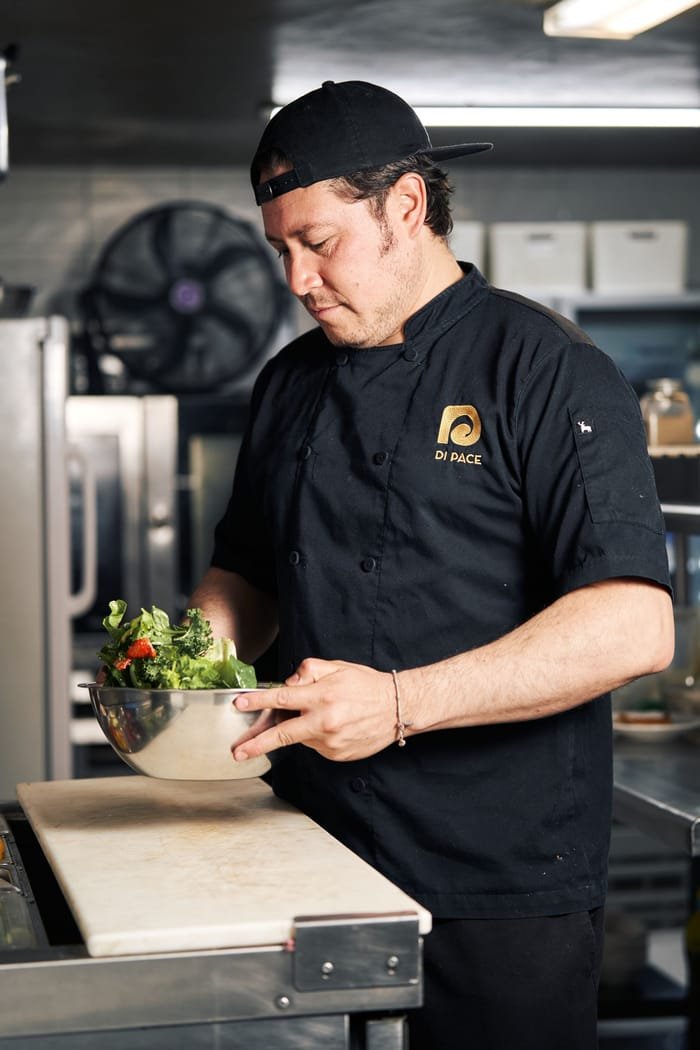 Chef de cozinha preparando salada fresca em uma bancada de inox de cozinha profissional