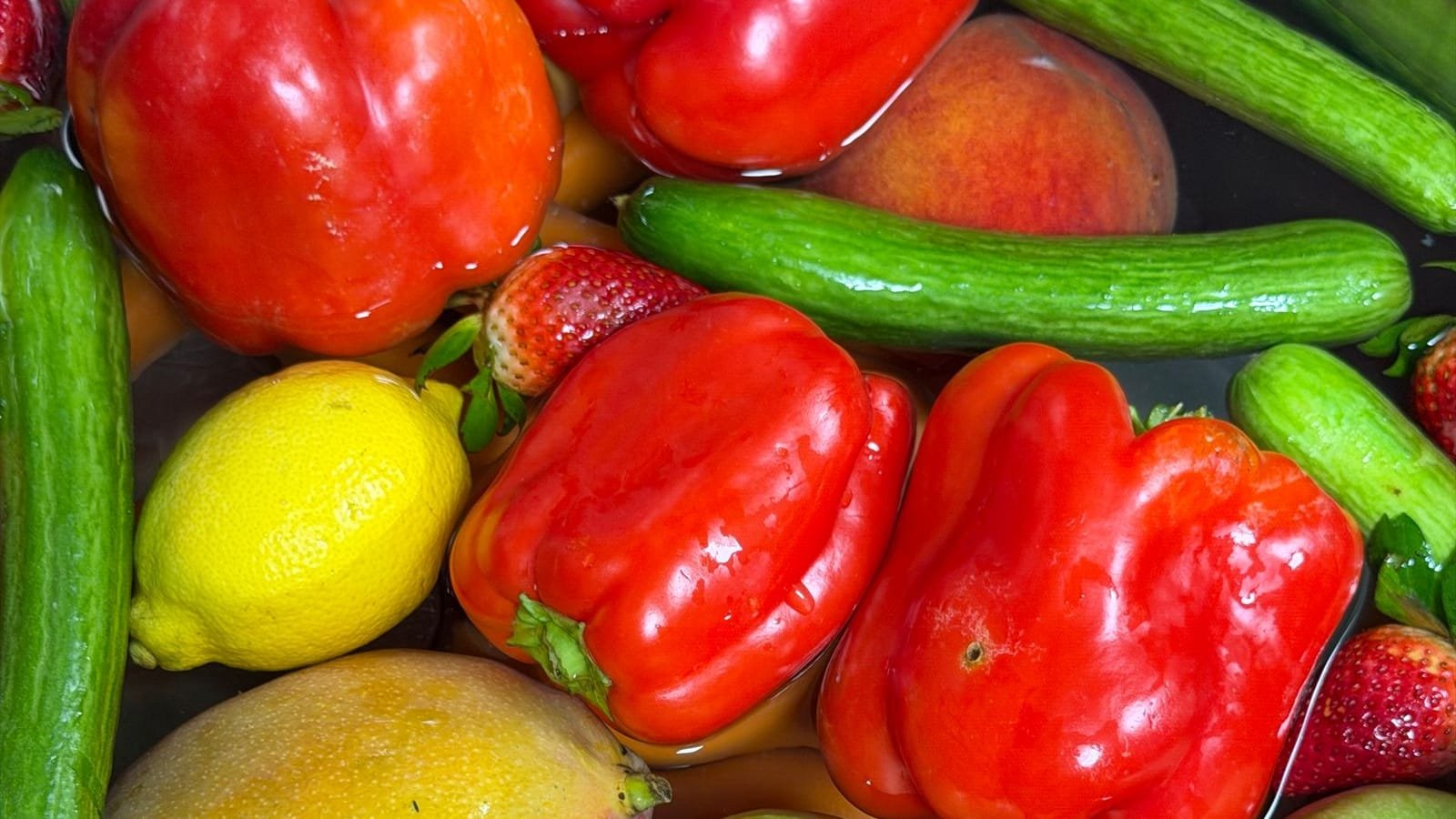 Pimentões vermelhos, pepinos, morangos, limão e frutas frescas imersos em água para higienização
