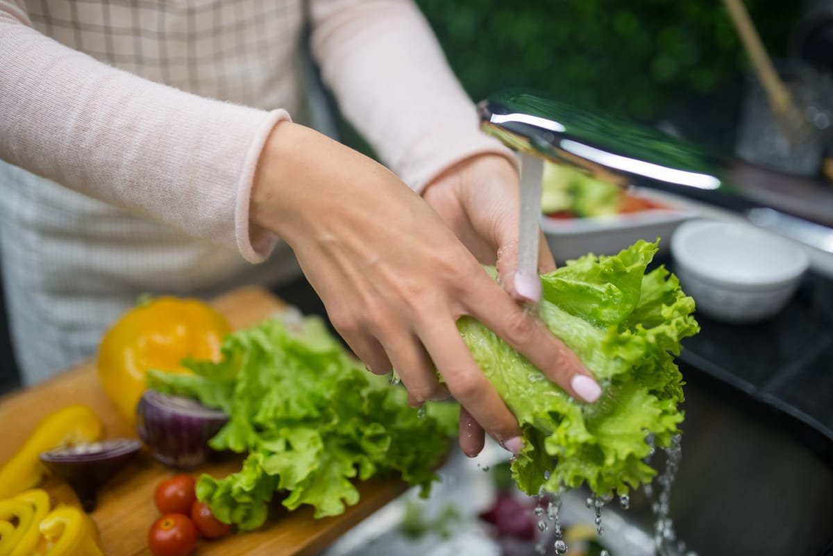 Mãos lavando folhas de alface sob água corrente na pia da cozinha
