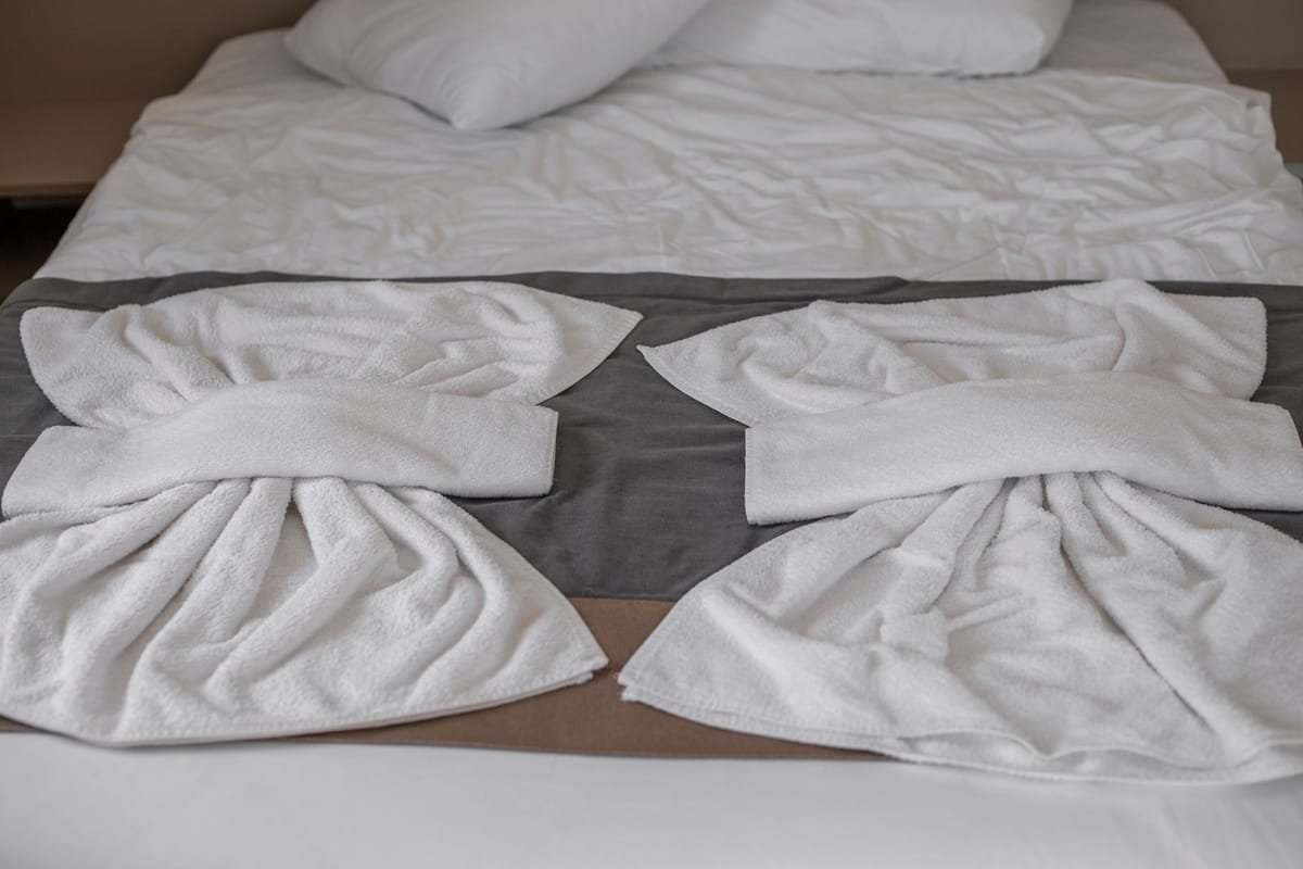 Quarto de hotel com cama arrumada e toalhas brancas dobradas em formato decorativo